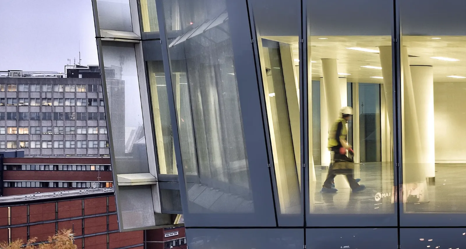 A site worker in a hard hat and hi-vis walking through a new glass-fronted office building
